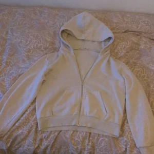 Ljus grå hoodie med dragkedja använd 4-5 gånger  - Säljer en beige hoodie med dragkedja och huva. Perfekt för en avslappnad stil. Den har långa ärmar och ribbade muddar vid ärmslut och nederkant. Enkelt och stilrent plagg för vardagsbruk.