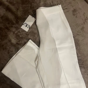 Vita kostymbyxor från Zara - Snygga vita kostymbyxor från Zara med en elegant och stilren design. Byxorna har en rak passform och är helt nya och oanvända. Lappen är kvar! Säljer på grund av fel storlek för mig tyvärr. 