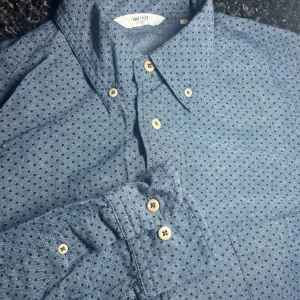 NN07 skjorta  - Snygg blå skjorta från NN07 med små prickar och klassisk krage. Skjortan har långa ärmar och knappar i en ljus kontrastfärg. Perfekt för en stilren look. Passar både vardag och på fest! Hör av dig vid minsta lilla fråga!🤩