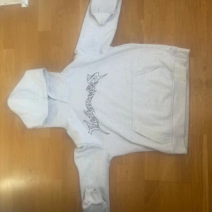 Grå hoodie från Vetements - Säljer en grå hoodie från Vetements med tryck på bröstet och ryggen. Hoodien har en klassisk passform med en stor ficka framtill och en bekväm huva. Perfekt för en avslappnad stil.