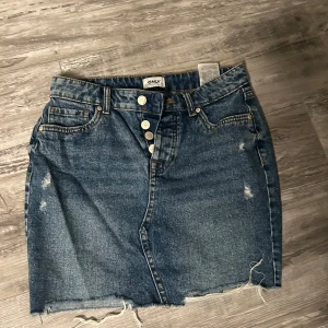 Jeanskjol från Only - Säljer en cool jeanskjol från Only med rå kant och slitna detaljer. Kjolen har knappar framtill och klassiska bakfickor. Perfekt för en avslappnad stil.
