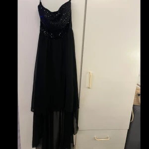 Svart axelbandslös klänning - Elegant svart axelbandslös klänning med glittrig överdel. Perfekt för festliga tillfällen med sin långa, flödande kjol och stilrena design.