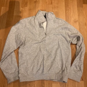 Grå tröja med dragkedja från H&M - Säljer en grå tröja från H&M i relaxed fit med halv dragkedja. Perfekt för en avslappnad stil. Tröjan har långa ärmar och är tillverkad i ett mjukt material.