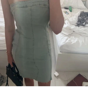 Jeans klänning  - Trendig  axelbandslös klänning i jeansmaterial. Perfekt för en somrig look med sin korta längd och figurnära passform. Klänningen har en stilren design med synliga sömmar som ger en cool touch.