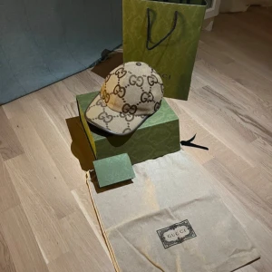 Beige keps från Gucci - Snygg beige keps från Gucci med det ikoniska GG-mönstret i brunt. Kepsen har en justerbar rem baktill och är tillverkad i ett slitstarkt material. Den är köpt på Guccis egna butik i Stockholm. Har alla orginala kvitton, boxar osv. Skriv till mig så skickar jag kvitoo mm.