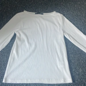 Vit ribbad topp - Säljer en stilren vit ribbad topp med slits ärmar. Perfekt för en enkel och snygg look. Toppen har en klassisk rund halsringning och är tillverkad i ett mjukt material. En liten smink fläck på ena armen men går att tvätta bort. 