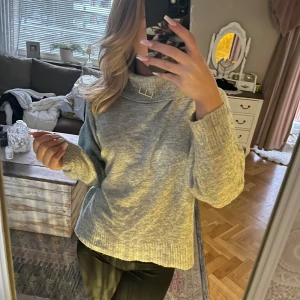 Grå stickad tröja med hög krage - Mysig grå stickad tröja med hög krage och långa ärmar. Perfekt för kyliga dagar och ger en stilren look. Passar bra till både jeans och kjol.