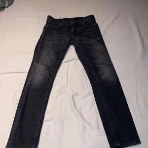 Svarta jeans från Nudie Jeans - Snygga svarta jeans från Nudie jeans i mörkgrå färg. De har en knappgylf och är tillverkade i slitstarkt denim. Perfekta för en stilren look. Storkek w29 L32