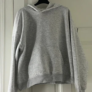 Grå hoodie från Gina  - Säljer den klassiska  grå hoodie från Gina. Den har en bekväm passform och är perfekt för kyligare dagar. Huvan ger extra värme. Den är även ganska ny och har inte använts mer än 1 gång 
