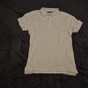 Grå pikétröja - Snygg grå pikétröja med klassisk krage och knappar. Perfekt för en avslappnad men stilren look. Kortärmad och i ett mjukt material som känns skönt mot huden.