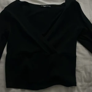 Svart omlottopp  - Elegant svart omlottopp.Perfekt för en stilren look. Toppen har en v-ringad design som ger en smickrande passform.