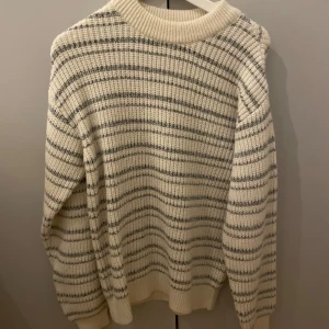 Randig stickad tröja från Pull&Bear - Säljer en mysig randig stickad tröja från Pull&Bear i krämvitt och grått. Tröjan har en rund hals och långa ärmar, perfekt för kyliga dagar. Passar bra till både jeans och kjol. 🧶