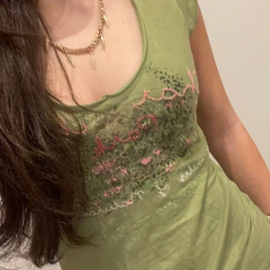 Grön t-shirt med tryck - Snygg vintage grön t-shirt med ett färgglatt tryck i rosa och andra nyanser. T-shirten har en rund halsringning och korta ärmar, perfekt för en avslappnad stil.