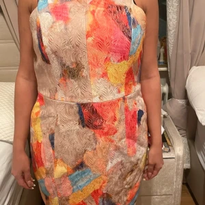 Färgglad klänning från H&M - Säljer en färgglad klänning från H&M med ett abstrakt mönster i orange, blått, rosa och beige. Klänningen har en figurnära passform och är ärmlös med en dragkedja i ryggen. Perfekt för en somrig look! 🌸 