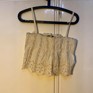 Beige axelbandslös topp från Zara - Säljer en söt beige axelbandslös topp från Zara med spetsdetaljer och broderade mönster. Perfekt för varma sommardagar. Toppen har en elastisk överdel för en bekväm passform.