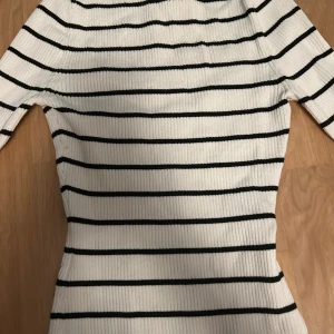 Randig ribbad tröja från H&M - Säljer en stilren vit och svart randig ribbad tröja från H&M. Tröjan har en fyrkantig halsringning och trekvartsärmar, perfekt för en chic look. Passar bra till både jeans och kjol!