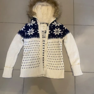 Vit och marinblå stickad kofta med snöflingemönster och pälsluva  - Trendig, mysig vit och marinblå stickad kofta från H&M med snöflingemönster. Den har en huva med fuskpäls och knappar framtill. Perfekt för kyliga dagar! Mycket bra skick!