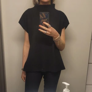 Svart stickad topp med hög krage  - Säljer en stilren svart stickad topp med hög krage och korta ärmar. Perfekt för lager-på-lager eller som den är. Enkelt att matcha med olika outfits.