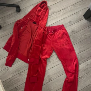 Röd velour hoodie från Juicy Couture - Säljer en snygg röd velour hoodie från Juicy Couture. Den har en dragkedja framtill och en mysig huva. Perfekt för en avslappnad stil med en touch av lyx. Passar perfekt till matchande byxor för en komplett look. Kan sälja ena delen också, kontakta isåfall. Original pris 2250. Använd endast 3-4 gånger