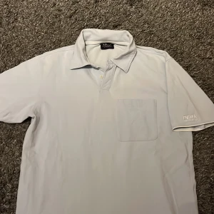 Ljusblå pikétröja från Peak Performance - Snygg ljusblå pikétröja från Peak Performance med klassisk krage och knappslå. Tröjan har en bröstficka och logotyp på ärmen. Perfekt för en avslappnad stil. Skriv gärna vid fler frågor!