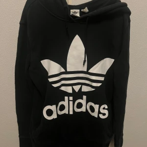 Svart hoodie från Adidas - Säljer en svart hoodie från Adidas i storlek XS. Den har den klassiska Adidas-loggan i vitt på framsidan Den används inte längre så jag vill bli av med den:)