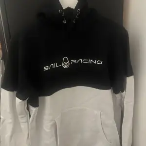 Säljer en snygg svart och vit hoodie från Sail Racing. Den har en stor logga på bröstet och en praktisk magficka. Perfekt för kyliga dagar eller som en stilren vardagströja. Passar både till jeans och träningsbyxor!