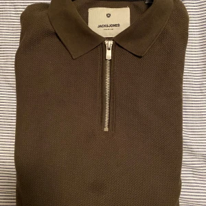 Brun pikétröja från Jack & Jones - Snygg brun pikétröja från Jack & Jones med dragkedja framtill. Perfekt för en stilren look, oavsett om det är till vardags eller fest. Tröjan har en klassisk krage och är i mycket bra skick. Passar perfekt till både jeans och chinos!