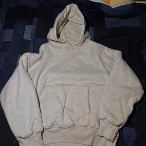 Rare yeezy hoodie - Säljer en grå hoodie från YZY med röd söm. Tillverkad i USA, denna hoodie har en klassisk design med huva och ribbade muddar. Otrolig rare. Aldrig sett nån annan online. Knappen på sista bilden kom så från fabrik tyvärr annars inga defekter.