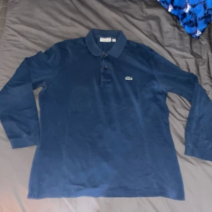 Mörkblå långärmad pikétröja från Lacoste - Snygg mörkblå pikétröja från Lacoste med långa ärmar och klassisk krage. Perfekt för en stilren look. 🐊