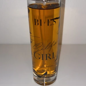 Selfie Girl Eau de Parfum - Säljer en elegant parfymflaska från Bies med doften Selfie Girl. Flaskan är hög och smal med en genomskinlig design som visar den gyllene vätskan inuti. Perfekt för den som vill ha en fräsch och ungdomlig doft. Passar både till vardags och fest!