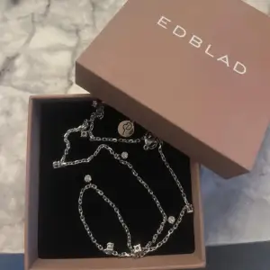 Elegant silverhalsband från Edblad med små dekorativa detaljer. Halsbandet har en tunn kedja och flera små hängen som ger en stilren look. Perfekt för att lägga till en subtil glans till din outfit.