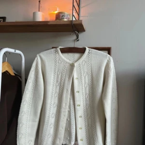 Vit söt stickad kofta med knappar - Säljer en elegant vit stickad kofta med ett subtilt mönster och knappar framtill. Perfekt för kyliga dagar och ger en stilren look. Det finns ingen lapp på men skulle säga att det är xs eller s. Liten fläck, se bild 3💖