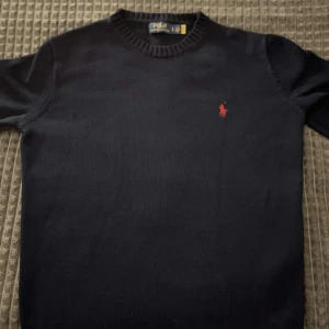 Polo Ralph Lauren stickad tröja - Säljer en stilren svart tröja från Polo Ralph Lauren i storlek S. Tröjan har en klassisk design med ett rött broderat logotyp på bröstet. Perfekt för både vardag och festliga tillfällen. Den är i mycket bra skick och redo för en ny ägare! Väldigt eftertraktad där den går för cirka 2199 kr. Använd några gånger därför är mitt pris 899 kr
