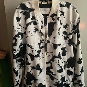 Svartvit bomberjacka från Galagowear - Snygg svartvit bomberjacka från Galagowear med ett unikt mönster, använt 1 gång, nyskick.Jackan har dragkedja framtill och broderade detaljer på ryggen. Perfekt för en cool och avslappnad stil.
