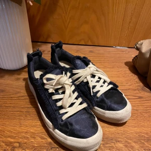 Svarta sneakers från Zara - Snygga svarta sneakers från Zara med vita snören och en unik fransdetalj längs kanterna. Skorna har en vit sula och är tillverkade i ett glansigt material som ger en stilren look.