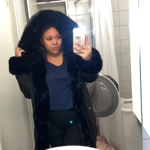 Svart dunjacka med pälsdetaljer - Säljer en snygg svart dunjacka med fluffiga pälsdetaljer runt huvan och längs med dragkedjan. Perfekt för kalla vinterdagar! Jackan är långärmad och har en stilren design som passar både till vardags och fest. Den är i mycket bra skick och håller dig varm och bekväm hela säsongen. Det är inte äkta päls och bara använd en vinter. Den har stor luva och är i storlek L men passar som M. Två fickor, en på varsin sida. Nypris 1800kr