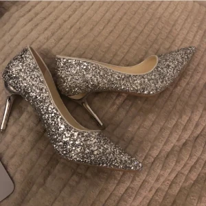 Glittriga silverpumps med spetsig tå - Säljer ett par fantastiska glittriga pumps i silver med spetsig tå och hög klack. Perfekta för festliga tillfällen när du vill glänsa lite extra. De är i bra skick men har några skador, som visas på bilderna. I storlek 37