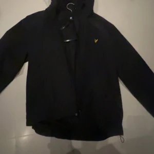 Windbreaker lyle scott  - Snygg svart jacka med huva och dragkedja. Jackan är stilren och passar till många olika outfits.Storlek M men passar även L