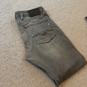 Grå jeans från Replay - Säljer ett par snygga grå jeans från Replay i mycket bra skick. De har en klassisk femficksdesign och en stilren grå färg som passar perfekt till alla tillfällen. Jeansen har en normal passform och är tillverkade i ett bekvämt material som ger en skön känsla hela dagen. Modellen är Anbass och köpta för 1499 kr.