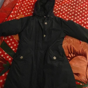 Svart parkajacka med huva - Säljer en svart parkajacka i damstorlek XS från GB. Jackan har en praktisk huva och stängs med både dragkedja och knappar. Perfekt för höst och vinter med sin långa ärm och stilrena design. Den är i bra skick och redo för nya äventyr!