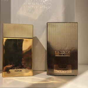 Tom Ford Noir Extreme Parfum - Elegant och lyxig parfym från Tom Ford i en gyllene flaska med räfflad kork. Doften är intensiv och sofistikerad, perfekt för den som vill sticka ut. Flaskan har en stilren design med märkets logotyp på toppen.