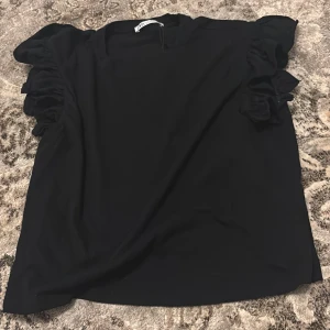 Svart blus med volangärmar - Elegant svart blus med volangdetaljer på ärmarna. Perfekt för en stilren look.