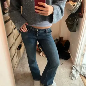 Säljer ett par snygga low waist blå jeans från Monki med bootcut-stil. De har dekorativa orangea broderier på bakfickorna och en klassisk femficksdesign. Perfekta för en avslappnad look. De är storlek 27 på monkis storleksguide, 