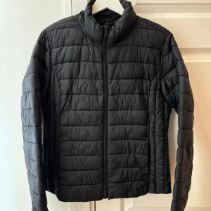 Svart quiltad jacka - Snygg svart quiltad jacka med dragkedja och hög krage. Perfekt för kyligare dagar med sin stilrena design och bekväma passform.