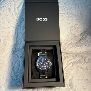 Klocka från BOSS - Säljer en klocka från BOSS i silver med en snygg blå urtavla. Klockan har en ädelstålarmband och kommer i originalförpackning. Helt ny med taggar kvar! Hör av er om ni undrar något.