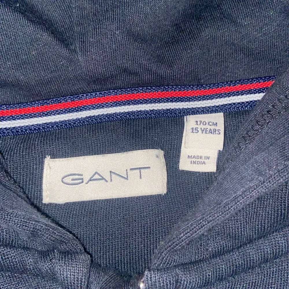 Säljer en klassisk svart hoodie från GANT i mycket bra skick. Den har en dragkedja framtill och en liten logga på bröstet. Perfekt för höst och vinter, och passar både till vardags och lite mer avslappnade tillfällen. Superbekväm och stilren! (Accepterar endast Swish pga lurendrejerier) (Checka även in andra kläder på min profil och köp tillsammans för ett rabatterat pris). Neuletakit & Villapaidat.