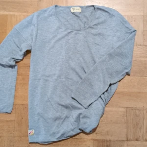 Ljusgrå långärmad tröja från About Knowing - Säljer en stilren ljusgrå långärmad tröja från About Knowing. Tröjan har en enkel design med rund hals och en liten färgglad etikett vid nederkanten. Perfekt för en avslappnad look.