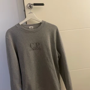 Grå sweatshirt från C.P. Company - Säljer en stilren grå sweatshirt från C.P. Company i mycket bra skick. Tröjan har en klassisk rund halsringning och långa ärmar. Perfekt för både vardag och avslappnade tillfällen. Passar bra till jeans eller chinos för en casual look.