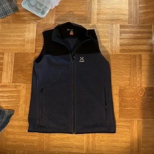 Blå och svart fleeceväst från Haglöfs - Säljer en svart och blå fleeceväst från Haglöfs i nyskick. Endast använd 1 gång. Nypris: 1400kr. Västen har en dragkedja framtill och två praktiska fickor med dragkedjor. Perfekt för lager-på-lager under kyliga dagar. Passar bra för både vardag och utomhusaktiviteter.