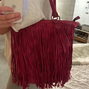 Rosa axelväska med fransar - supercool rosa axelväska i mocka med långa fransar. Väskan har två handtag och är i mycket bra skick!